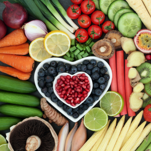 Color vegetables and fruit with some fruit in a heart-shaped bowl.